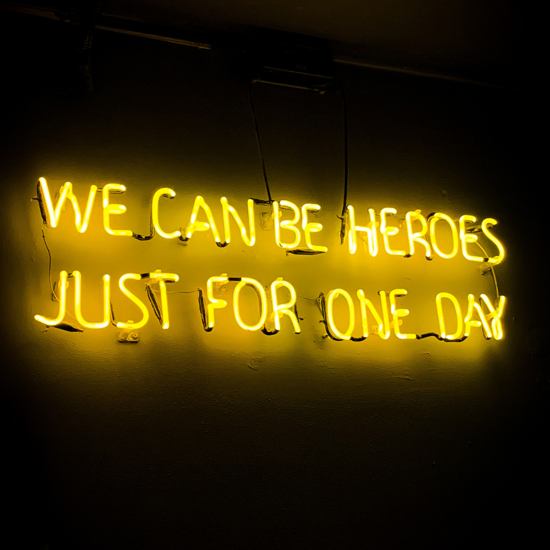 neon sign in yellow that says &quot;we can be heroes just for one day&quot;